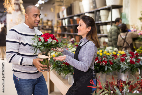 Woman owner of flower shop advising male customer before purchase of flowers