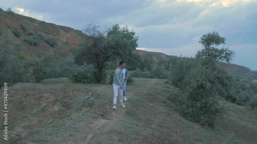 the girl runs along the hills with greenery for the guys, catches up and jumps on the guy's back, the couple laugh and have fun the girl runs along the hills with greenery for the guys, catches up and jumps on the guy's back, the couple laugh and have fun