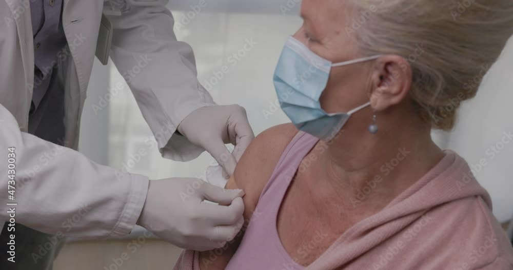Medical worker sticking adhesive bandage plaster on the hand of senior patient after vaccination. Elderly woman receiving vaccine against coronavirus, influenza, flu or pneumonia Medical worker sticking adhesive bandage plaster on the hand of senior patient after vaccination. Elderly woman receiving vaccine against coronavirus, influenza, flu or pneumonia