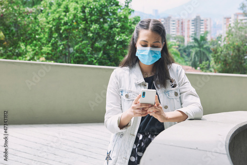 An attractive Hispanic female in a facial mask walking in an outdoor - photo