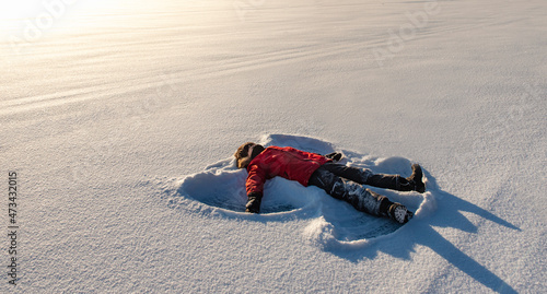 Child making a snow angel in an open snowy field in the morning sun. photo