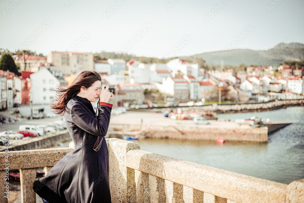 Brunette woman in dark coat taking photos from the top of a viewpoint Brunette woman in dark coat taking photos from the top of a viewpoint
