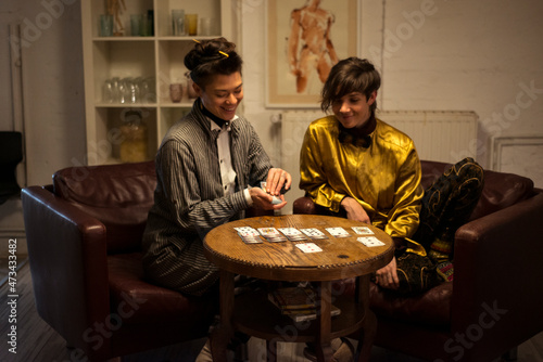 friends play cards at home dinner party on armchairs and laugh photo
