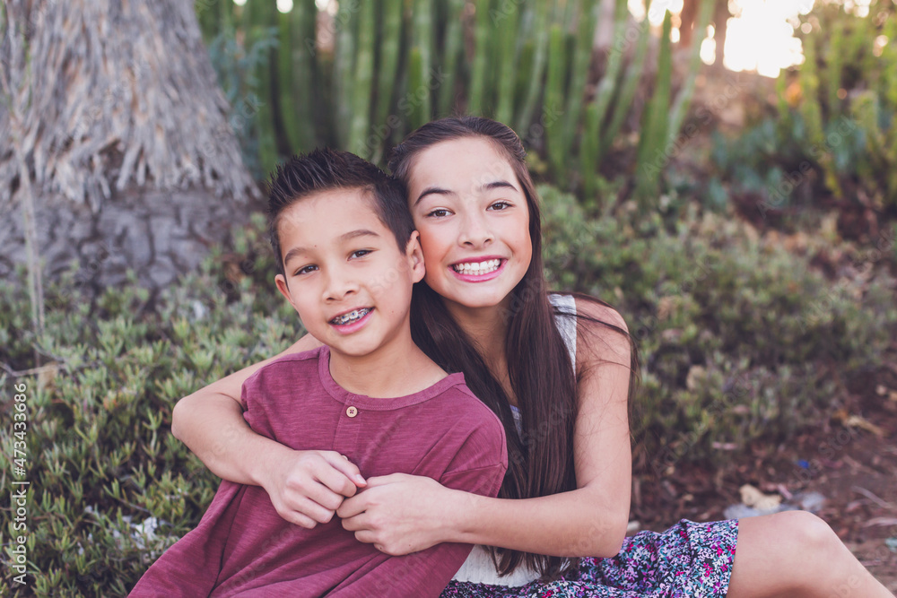 Older sister hugging young brother by a cactus garden Older sister hugging young brother by a cactus garden