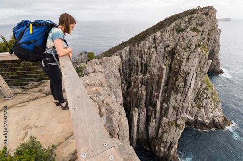 Woman leans over handrail on top of sea cliff in Tasman National Park. photo