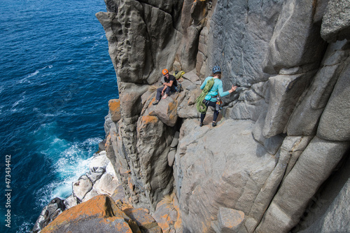 A couple of intrepid rockclimbers explore the featured sea cliffs of Cape Raoul, smiling at each other as they traverse the exposed terrain above a seal colony, in Tasmania, Australia. photo