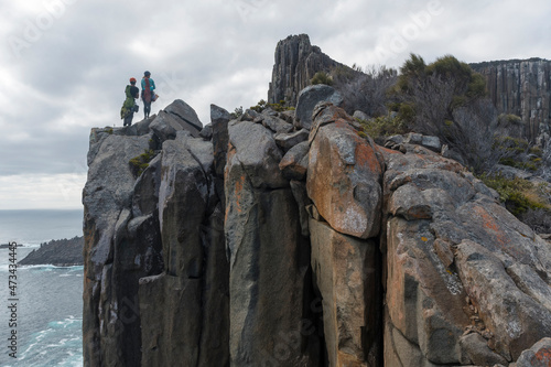 A couple of adventurers armed with ropes and climbing gear scope out their next challenge as they rockclimb the sea cliffs of Cape Raoul, Tasmania, Australia. photo