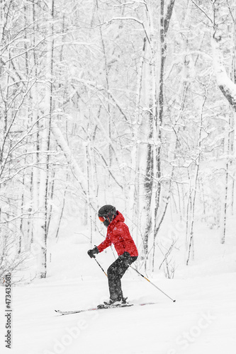 Alpine skiing. Woman skier going dowhill fast against snow covered trees background during winter snowstorm. Woman in red jacket and goggles. Winter wonderland