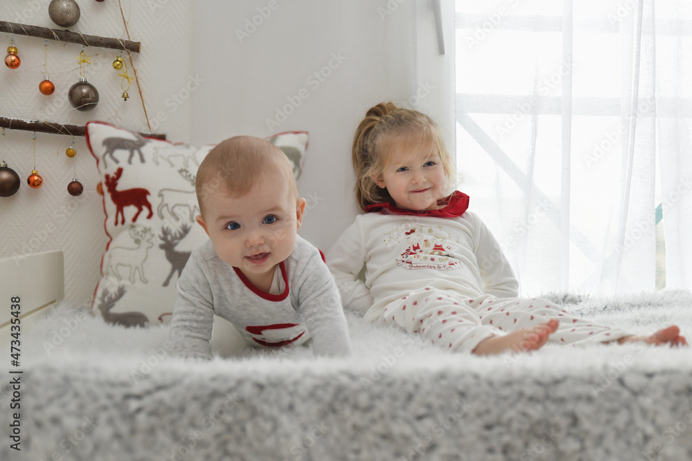 Brother and sister in Christmas pajamas are sitting on the bed. Brother and sister in Christmas pajamas are sitting on the bed.