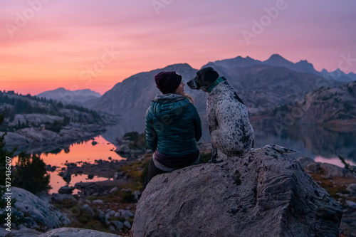 Rear view of young woman sitting on rock with dog on mountain during sunset
