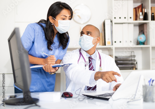 Doctor and nurse in protective medical mask check patient data in hospital computer database