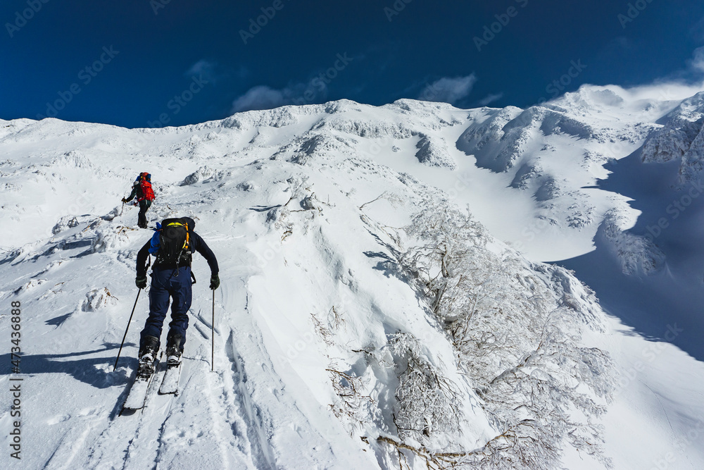Low angle view of people with splitboards and backpacks climbing snowcapped mountain Low angle view of people with splitboards and backpacks climbing snowcapped mountain