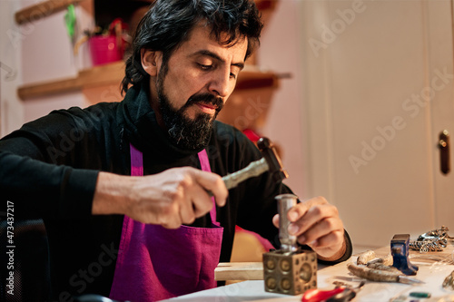 Jeweler craftsman hitting a metal plate with the hammer on the work table inside the workshop photo