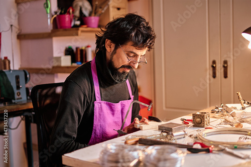 Jeweler craftsman cutting a metal plate with a saw at the work table inside the workshop