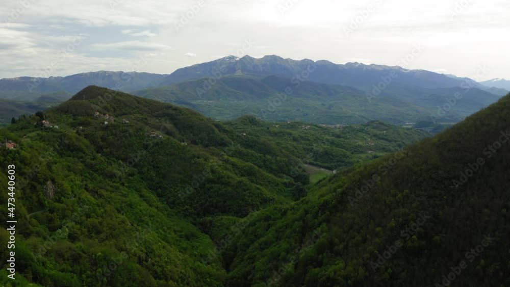Aerial Forward Built Structures On Green Mountains Against Cloudy Sky - Apennine Mountains, Italy