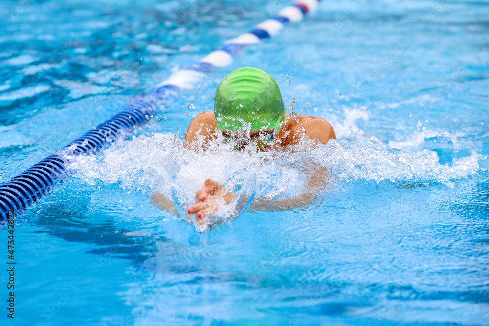 Unrecognizable breaststroke swimmer in a race, focus on water splash