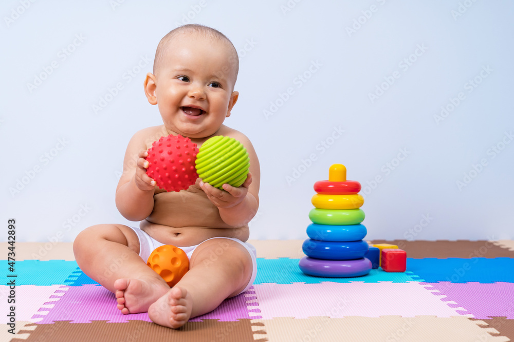Happy newborn baby plays with rubber balls in the playroom. Development of hand motor skills in children Happy newborn baby plays with rubber balls in the playroom. Development of hand motor skills in children