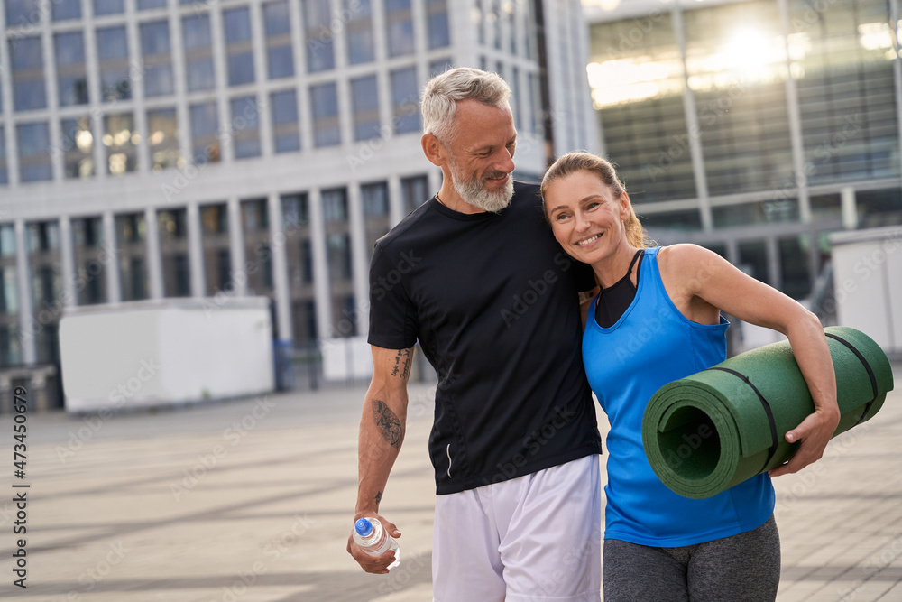 Portrail of sporty mature couple, man and woman in sportswear walking together in the city after morning training Portrail of sporty mature couple, man and woman in sportswear walking together in the city after morning training
