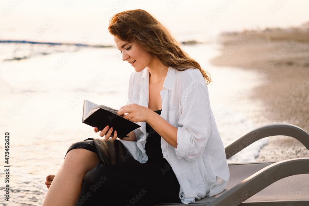 Woman holds book in her hands. Reading the book on a sea during beautiful sunset.