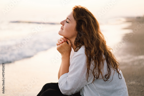 Woman closed her eyes, praying on a sea during beautiful sunset. Hands folded in prayer concept for faith, spirituality and religion. Peace, hope, dreams concept photo