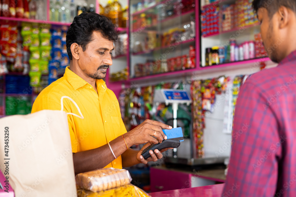 Indian customer making payment using credit card at groceries or Kirana shop - concept of digital or cashless payment, finance and Small business. Indian customer making payment using credit card at groceries or Kirana shop - concept of digital or cashless payment, finance and Small business.