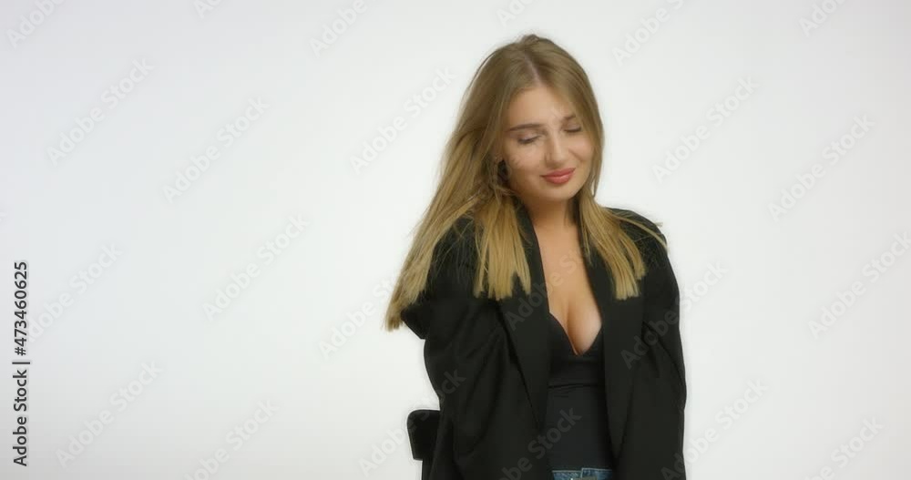 Beautiful young woman poses in the studio in front of the camera on a white background. A model Caucasian girl with long blonde hair in a black shirt smiles and is embarrassed. Beautiful female face Beautiful young woman poses in the studio in front of the camera on a white background. A model Caucasian girl with long blonde hair in a black shirt smiles and is embarrassed. Beautiful female face