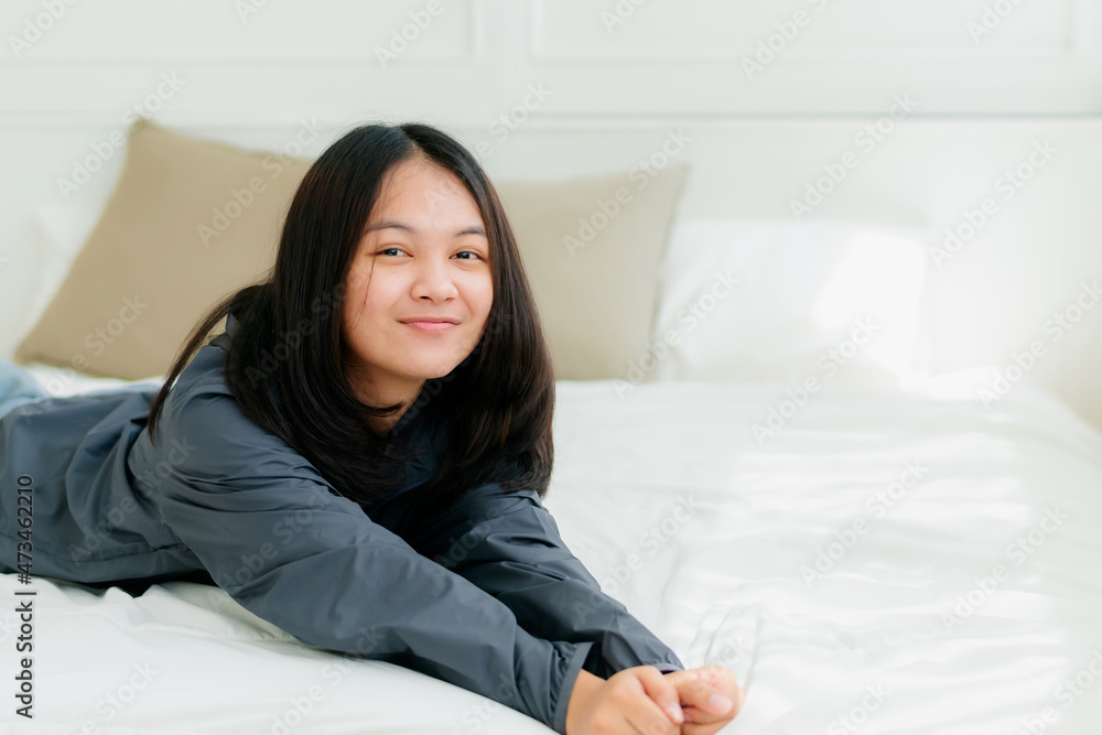 Portrait Asian cute long-haired teen wearing a gray long sleeve shirt Lay back and relax in bed in the bedroom happily. Portrait Asian cute long-haired teen wearing a gray long sleeve shirt Lay back and relax in bed in the bedroom happily.