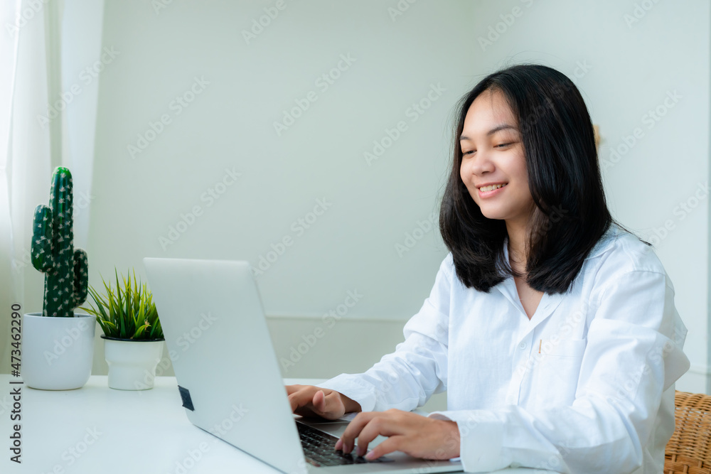 Portrait Cute Asian teen with long hair Wearing a white shirt, sitting happily studying online with a laptop on the bedroom desk. Portrait Cute Asian teen with long hair Wearing a white shirt, sitting happily studying online with a laptop on the bedroom desk.