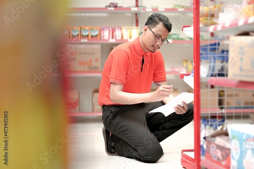  an employee of a supermarket wear uniform stocks shelves with checking goods for report about the inventories.