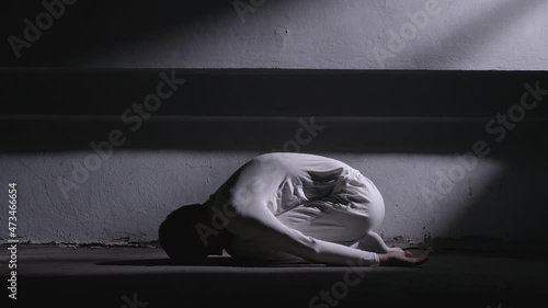 Mad man in white clothes lying in fetal position and getting up photo