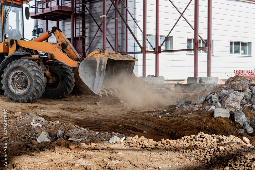 A powerful front loader on a construction site clears up the battle after dismantling reinforced concrete structures. Moving soil with construction equipment. Excavations. A powerful front loader on a construction site clears up the battle after dismantling reinforced concrete structures. Moving soil with construction equipment. Excavations.