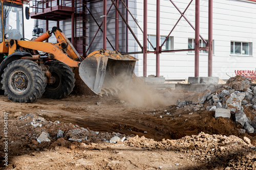 A powerful front loader on a construction site clears up the battle after dismantling reinforced concrete structures. Moving soil with construction equipment. Excavations.