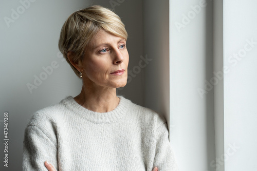 A thoughtful middle-aged woman looks out the window and is sad