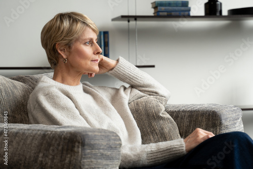 A middle-aged woman is sitting alone in an armchair and looking at the view from the window. photo