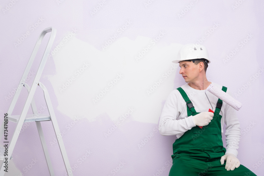 a worker with a paint roller looks at a white piece of wall a worker with a paint roller looks at a white piece of wall