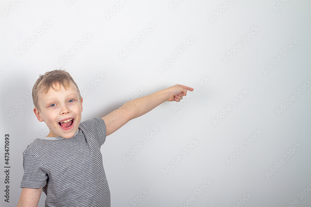 Cheerful caucasian boy smiles and points with his finger on a gray background Cheerful caucasian boy smiles and points with his finger on a gray background