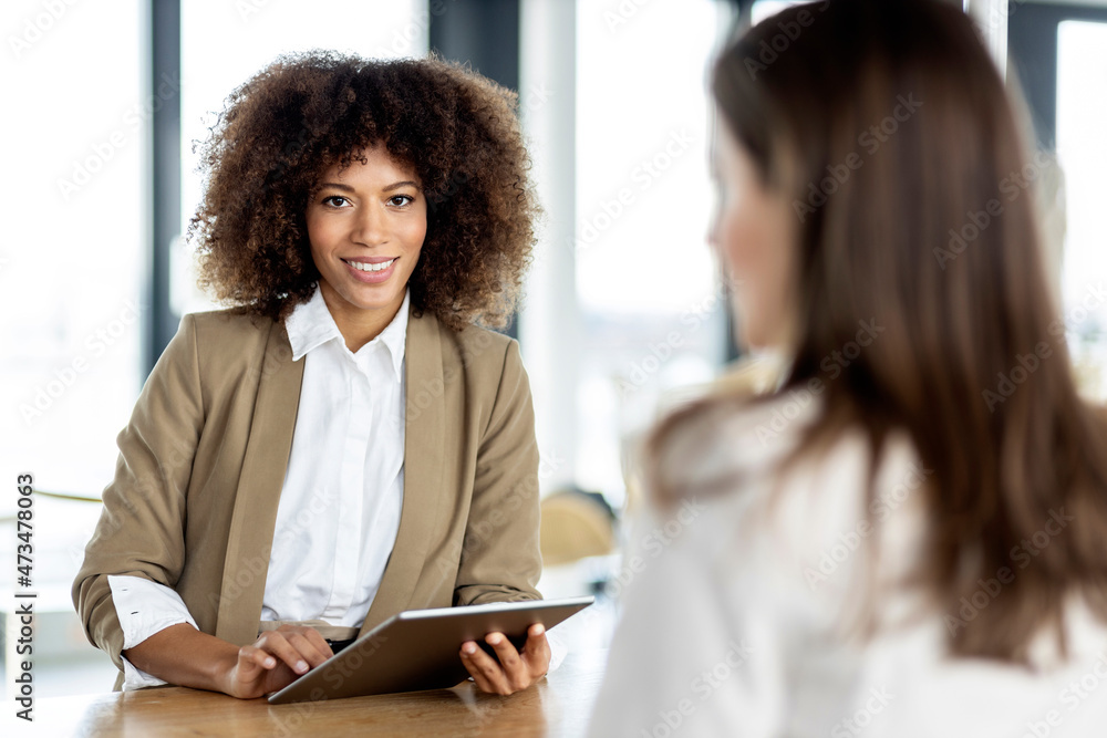 Smiling businesswoman holding digital tablet while standing with colleague in office Smiling businesswoman holding digital tablet while standing with colleague in office