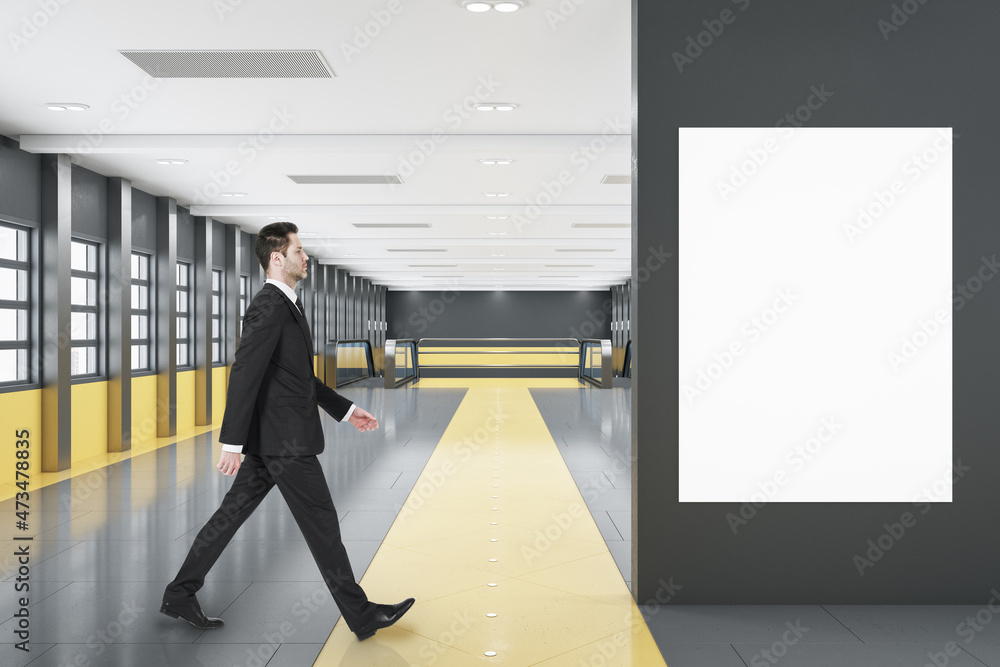 Fototapeta premium Businessman walking in modern black and orange tile shopping mall or airport interior with empty white mock up poster on wall, windows, city view and escalator. Public area concept.