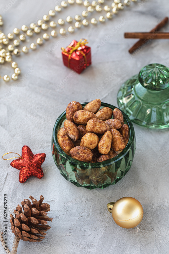 Candied or sugared almonds with honey and cinnamon in trendy green small glass jar on gray with Christmas decoration background. Traditional Christmas sweets for holidays. Copy space Candied or sugared almonds with honey and cinnamon in trendy green small glass jar on gray with Christmas decoration background. Traditional Christmas sweets for holidays. Copy space