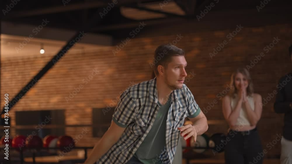 Young Male Bowling Player Throws a Ball with the Support of Friends and Rejoices by Knocking Out a Shake Young Male Bowling Player Throws a Ball with the Support of Friends and Rejoices by Knocking Out a Shake