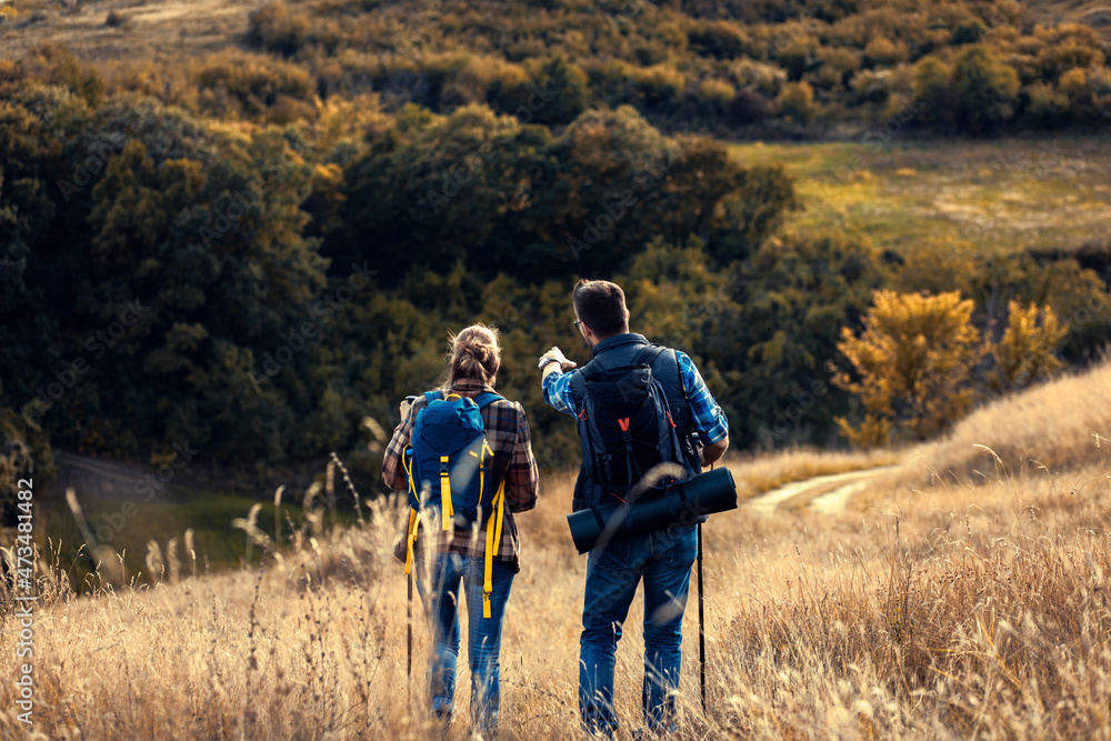 Rear view of couple with backpacks hiking together in nature on autumn day. Rear view of couple with backpacks hiking together in nature on autumn day.