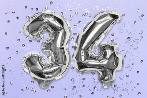 Silver foil balloon number, digit thirty four on a lilac background with sequins. Birthday greeting card with inscription 34. Top view. Numerical digit. Celebration event, template. photo