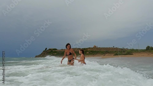 Mother and daughter playing with big waves at Marinella of Selinunte beach under archaeological park in Sicily, Italy. Slow-motion photo