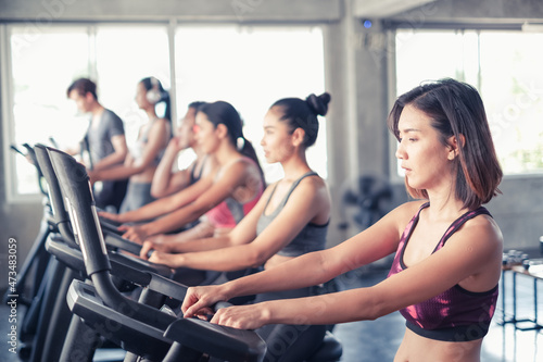 group friends working out on exercise bike and wearing sportswear in fitness or gym center, strength sporty and weight loss concept