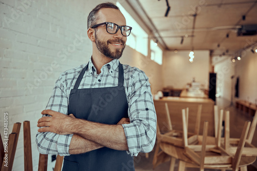 Foto Joyful bearded man in apron standing in cafe