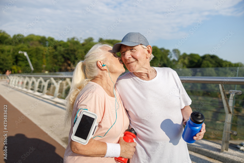 Mature woman kisses happy husband with cap at training on city footbridge