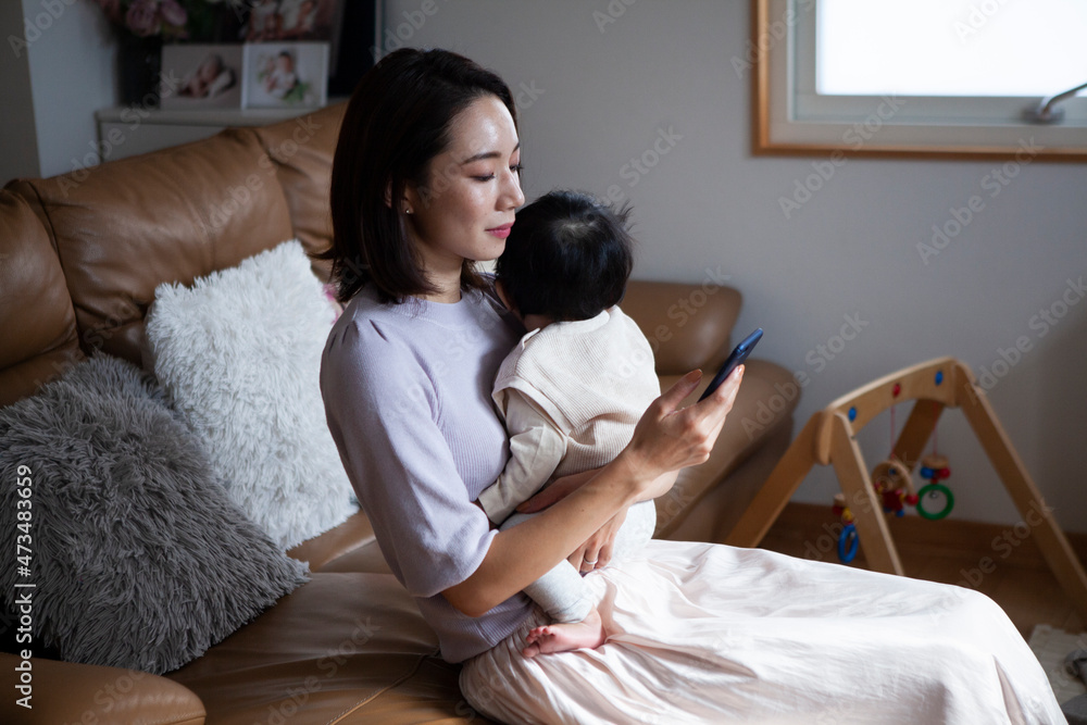 赤ちゃんを抱きながらスマートフォンを操作する女性 赤ちゃんを抱きながらスマートフォンを操作する女性