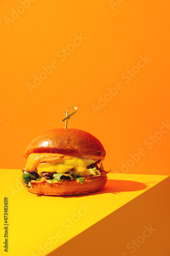 Big burger with cheese on bright orange and yellow background. American Fast food cuisine in a modern style.