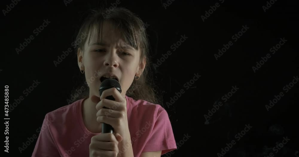 The teenager sings. Girl teenager girl singing into a microphone on a dark background. The teenager sings. Girl teenager girl singing into a microphone on a dark background.