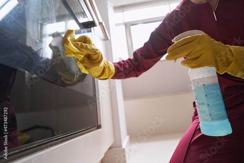 Professional housecleaner in rubber gloves cleaning part of electric cooker photo